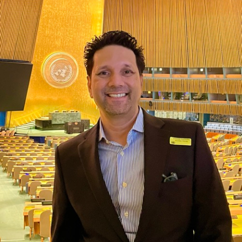 A man standing in the UN assembly hall looking at the camera.