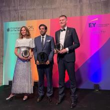 A woman and two men stand in front of a backdrop with awards in their hands.