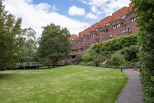 A red brick college building seen from the gardens
